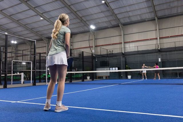 Women competing in indoor padel match on vibrant blue court demonstrating teamwork