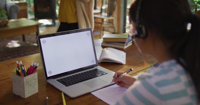 Student participating in online class from home. Laptop screen is blank, indicating possible use for design or online class demonstration. Perfect for articles on remote education, online learning methods, and working from home setups.