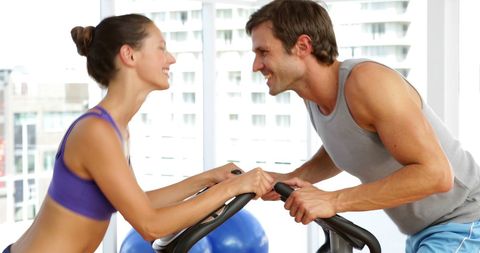 Fit Couple Exercising Together on Stationary Bikes at Gym
