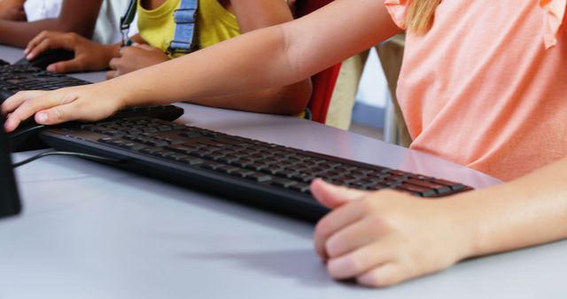 Children in a classroom using computers, focusing on a girl operating a keyboard. Suitable for educational content, technology integration in schools, promoting digital literacy for young learners, or illustrating classroom activities involving computers.