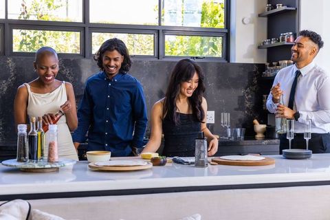Diverse friends laughing and preparing food at sunlit modern kitchen island