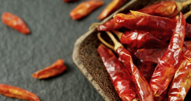 Dried red chili peppers spill from a rustic burlap sack onto a dark textured surface, with copy space. These fiery ingredients are essential in various cuisines for adding heat and flavor to dishes.