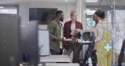Diverse team collaborating with laptop and tablet in modern open office with digital overlays