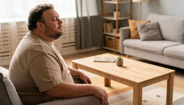 Contemplative man resting on armchair in cozy living room with wooden coffee table
