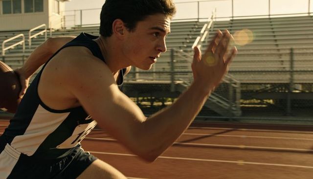Male sprinter charging from blocks on red track at golden hour