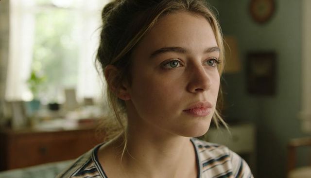 Young woman gazing out window in soft natural light at home, thoughtful closeup portrait