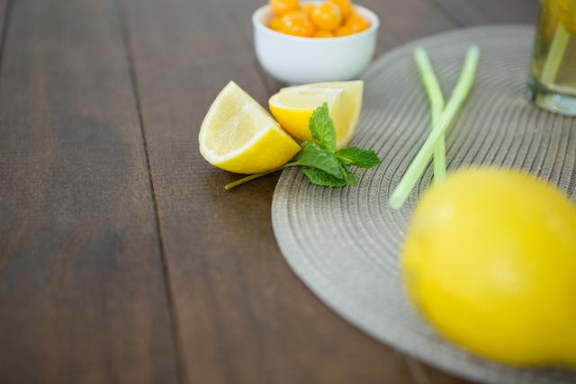 This image captures fresh lemon wedges and mint leaves on a wooden table, perfect for illustrating recipes, healthy eating, or natural ingredients. Ideal for use in food blogs, cooking websites, or health and wellness articles.