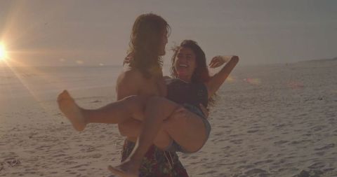 Beach Sunset Romance: Man Carrying Woman in Playful Embrace