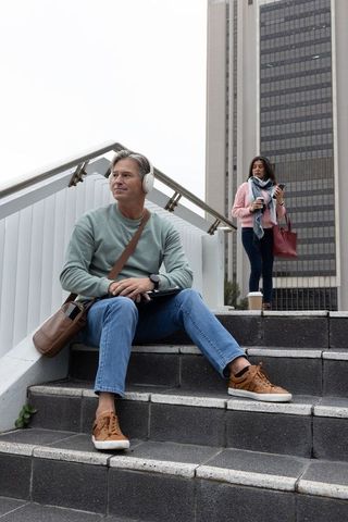 Urban commuters taking break on steps with headphones, tablet and coffee by office tower