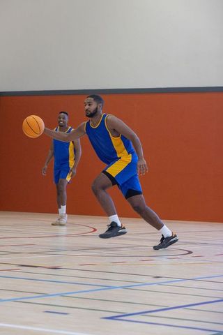 Teammates Dribbling Basketball on Indoor Court in Blue-Yellow Uniforms