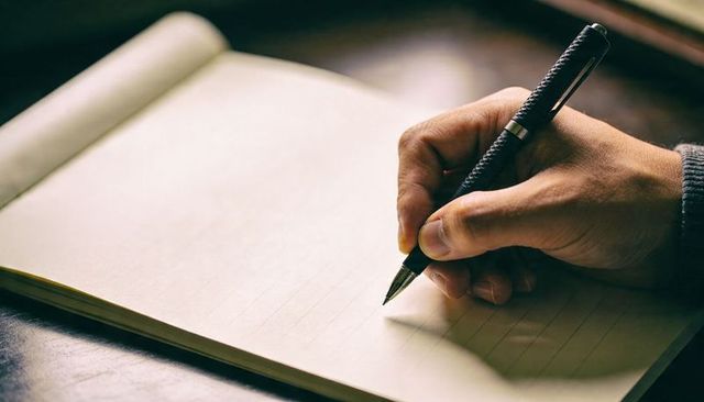 Right Hand Writing on Cream Lined Notebook with Black Pen and Warm Desk Light Ambience