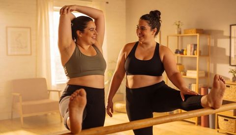 Plus-size women stretching at home ballet barre smiling during partner fitness routine