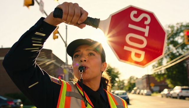 Uniformed traffic officer holding red stop paddle blowing whistle wearing reflective vest