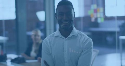 Confident professional smiling with arms crossed in open-plan office, sticky notes on glass
