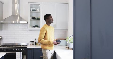 Man Looking Thoughtful in Modern Kitchen with Smartphone