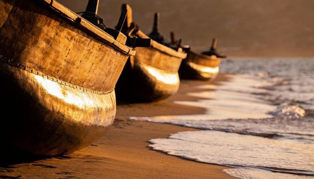 Golden hour wooden boats resting on wet sand with foamy surf