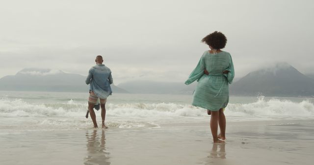 Couple Enjoying Walk on Beach with Mountain Background - Download Free Stock Images Pikwizard.com