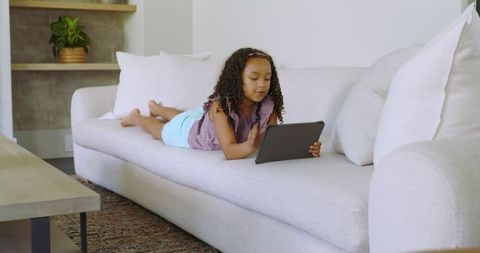 Young girl relaxing on sofa using tablet in modern living room