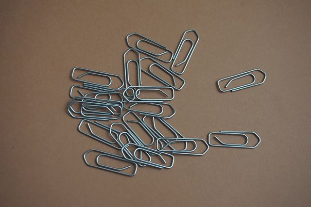 Metal paperclips scattered on brown surface. Ideal for themes of office organization, school supplies, workplace resources, and administrative concepts.