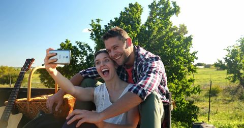 Happy Couple Taking a Selfie Outdoors with Guitar and Picnic