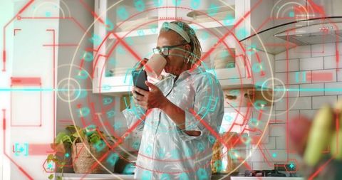 Senior woman using smartphone and sipping coffee in modern kitchen with digital hud overlay