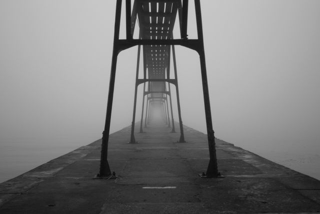 Empty pier disappearing into dense fog, creating a mysterious and tranquil atmosphere. Monochromatic tones enhance the sense of mystery and calmness. Ideal for use in design projects that need a touch of intrigue or a sense of solitude, as well as for backgrounds and storytelling visuals.