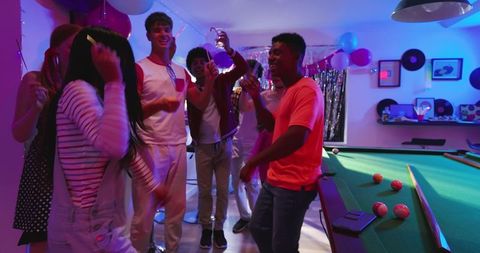 Young friends laughing and dancing in colorful basement lounge with pool table and smartphone