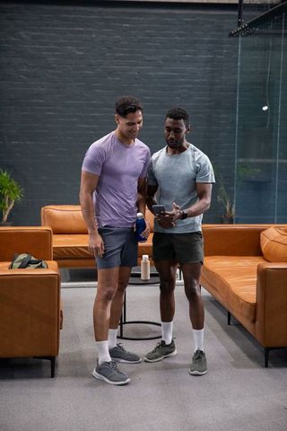 Sharing workout stats on smartphone, two men in gym lounge wearing activewear