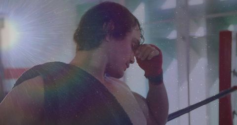 Weary boxer leaning on ropes rubbing face with red hand wrap towel over shoulder