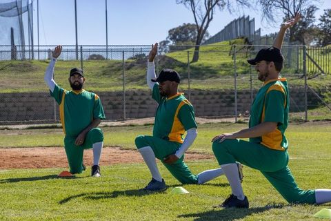 Lunging Baseball Players Performing Dynamic Warmup on Grass Field with Training Cones