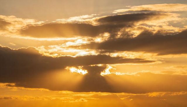 Golden crepuscular rays breaking through dramatic sunset clouds casting warm horizon light