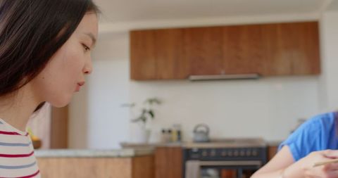 Asian family sharing meal at home using chopsticks at kitchen island