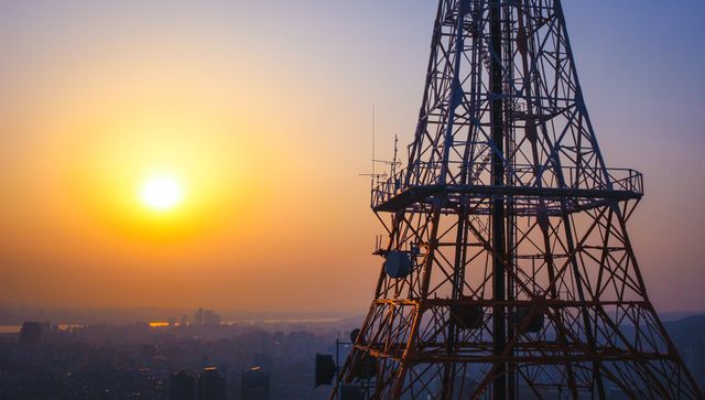 An image showcasing a sunset view from the top of a communications tower overlooking a cityscape. This photo emphasizes the contrast between the technological infrastructure and the natural beauty of the setting sun. Perfect for illustrating concepts related to telecommunications, urban life, and the intersection of technology and nature.