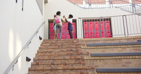 School Friends with Backpacks on Brick Staircase by Red Lockers Outdoors
