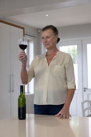 Senior Woman Evaluating Quality of Red Wine in Modern Kitchen