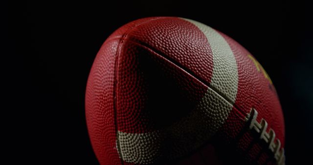 Close-up shot of an American football with textured leather surface and white laces on a black background. Useful for articles, promotional materials, or graphics related to sports, football season, team sports, or athletic equipment. Highlights details suitable for a focus on grip and design features.