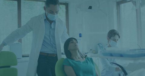 Female patient reclining in dental chair with masked dentist and assistant preparing tray