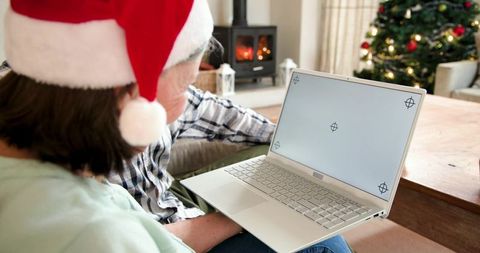 Senior couple wearing santa hat using laptop by cozy fireplace and christmas tree