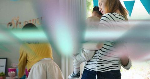 Mother cradling baby at pastel baby shower holding infant amid decorations and gifts