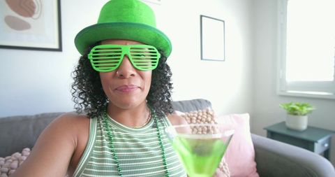 African american woman celebrating holiday wearing green hat holding emerald cocktail