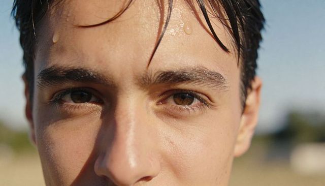 Sunlit closeup teen male face with sweat droplets and wet hair during golden hour outdoors
