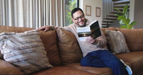 Mature asian man relaxing on sofa reading magazine at home