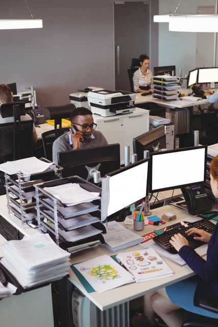 High angle view of a busy office environment with focused employees working at their desks. Ideal for illustrating corporate culture, teamwork, productivity, and modern business settings. Useful for business presentations, articles on office dynamics, and promotional materials for office supplies or corporate services.