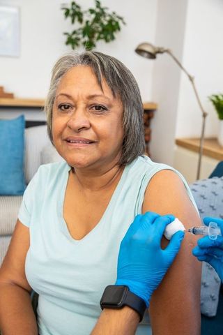 Senior woman receiving vaccination at home for health prevention