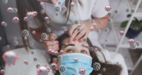 Masked esthetician tinting eyebrows during pandemic with visible airborne virus particles