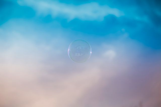 Captivating view of a single bubble floating against a soft, dreamy gradient sky transitioning from blue to pink. Perfect for concept works around childhood, imagination, freedom, or graphic design elements requiring a whimsical or peaceful background.
