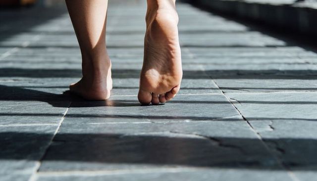 Bare feet walking on sunlit stone tiles with slatted shadows and grout lines