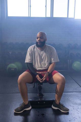 Man resting on bench between sets wearing compression sleeve in gym