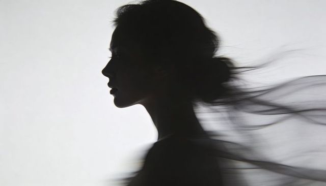 Backlit female profile silhouette with flowing sheer fabric and hair bun