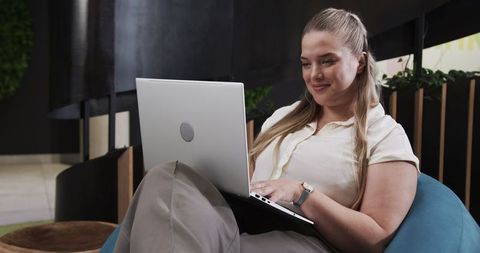 Woman relaxing in modern office lounge working on laptop